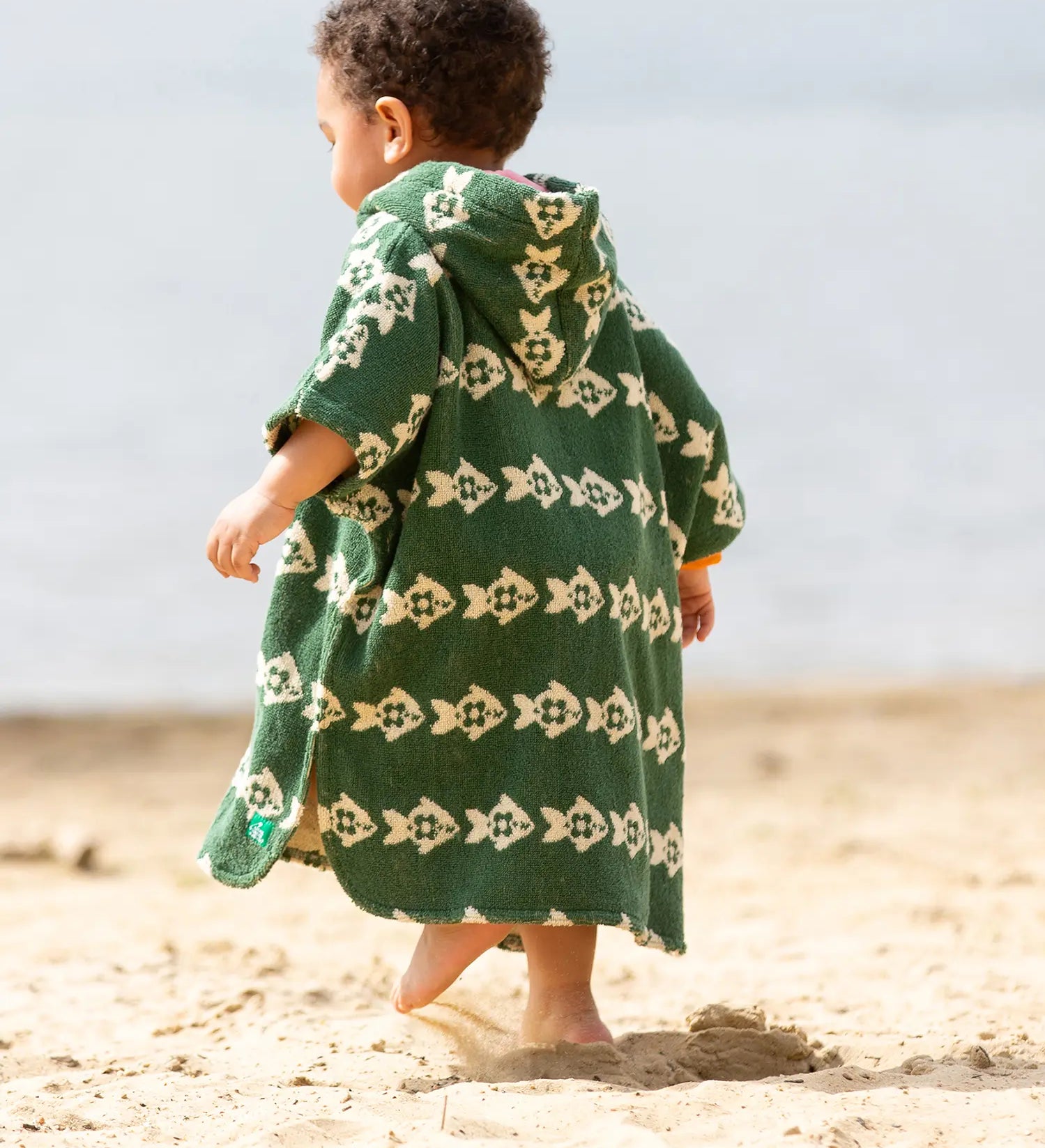 Back of a child wearing the Little Green Radicals swimming fish organic cotton hooded towel poncho. Cream fish pattern on a green background.
