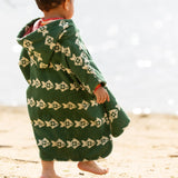 Back of a child wearing the Little Green Radicals swimming fish organic cotton hooded towel poncho, the hood has a pink coloured hood lining. Cream fish pattern on a green background.
