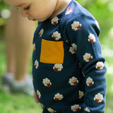 A close up of a child wearing the Little Green Radicals Kids' Organic Top and Joggers Playset with sleeping sheep print. The top has a yellow gold coloured chest pocket.  Little green Radicals have a wide range of organic cotton, Fairtrade children's clothing an outerwear available here at Babipur.