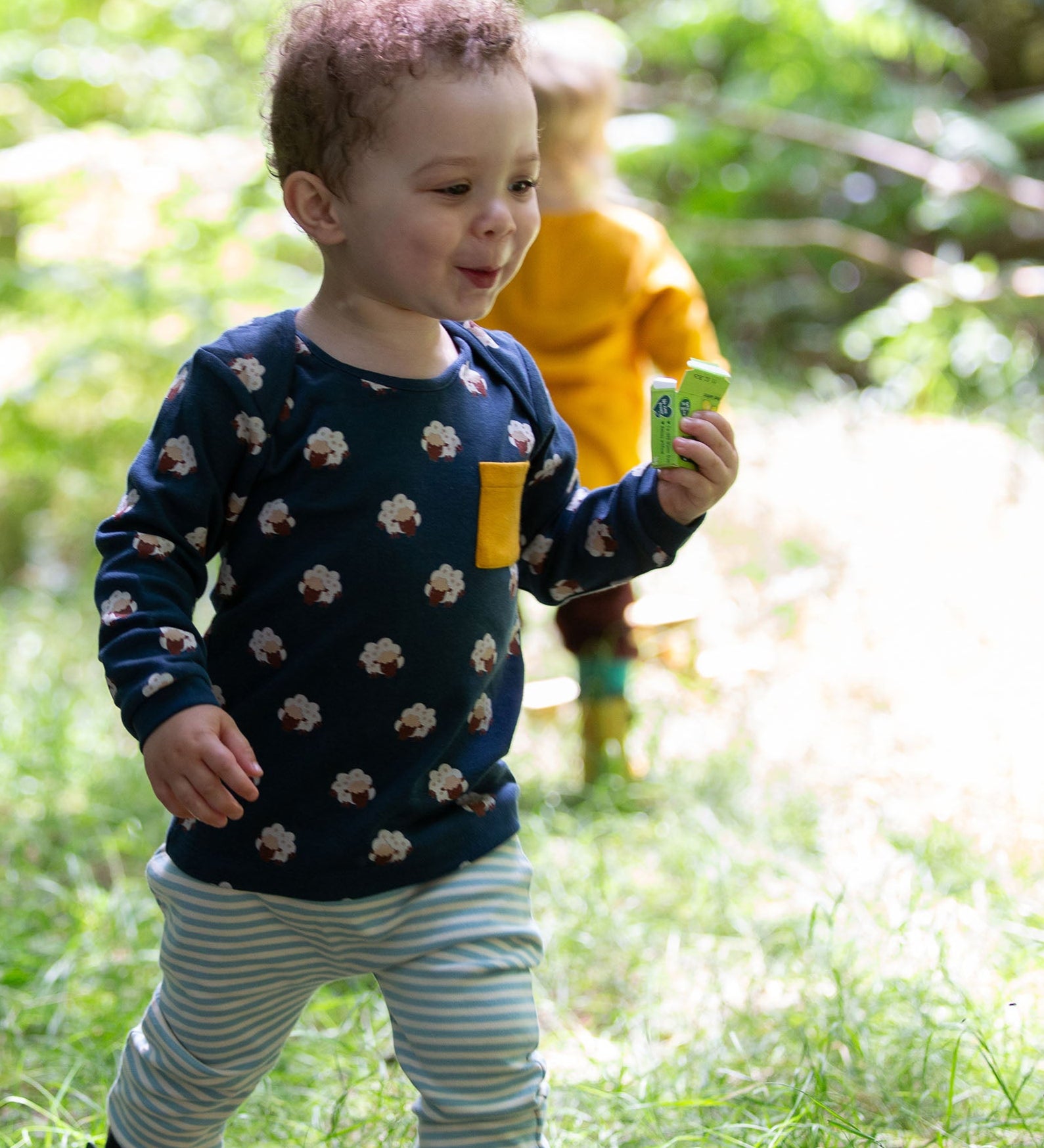 A child wearing the Little Green Radicals Kids' Organic Top and Joggers Playset featuring the Sleeping Sheep print on the top and a blue and white stripe on the joggers.  Little green Radicals have a wide range of organic cotton, Fairtrade children's clothing an outerwear available here at Babipur.