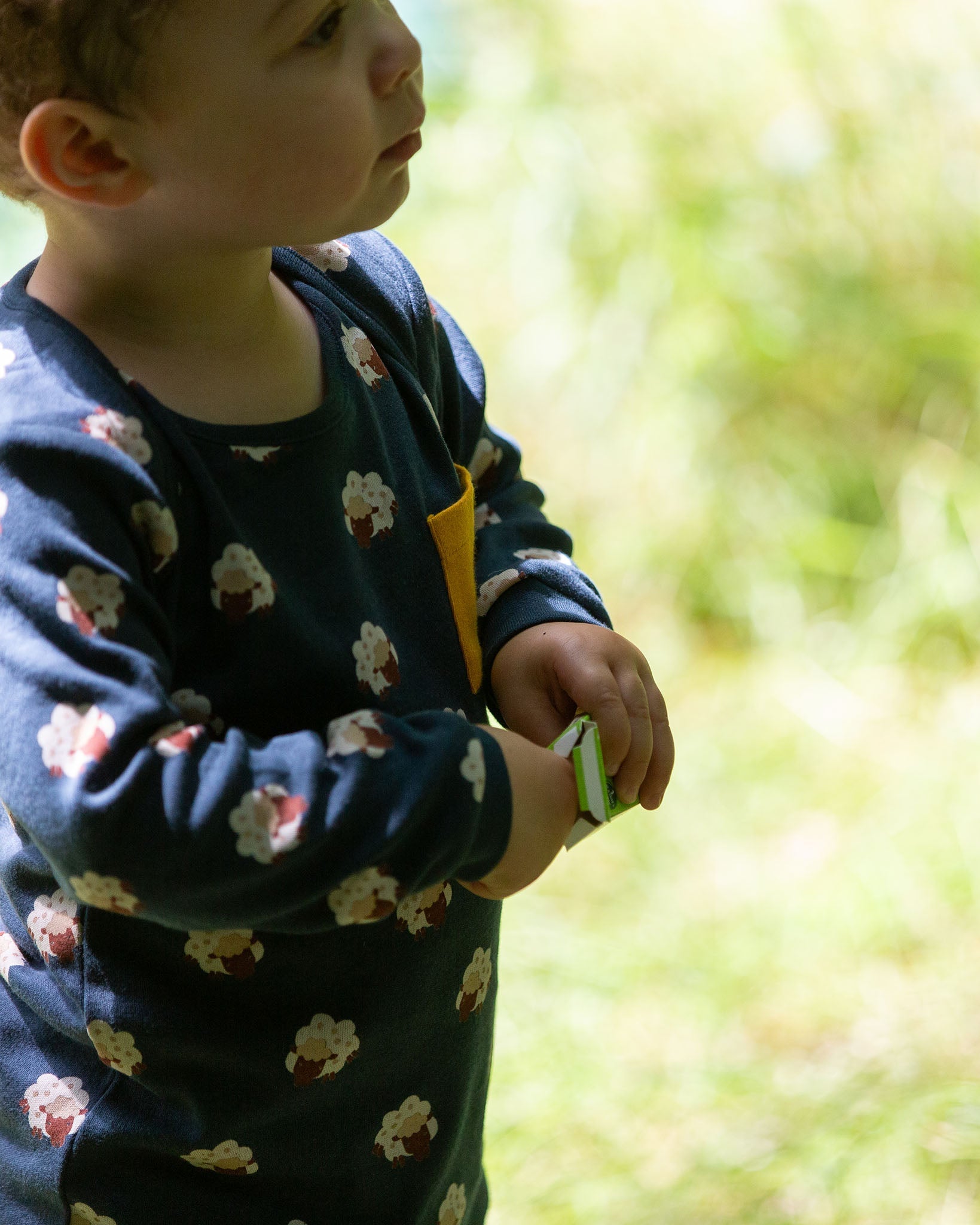 A close up of a child wearing the Little Green Radicals Kids' Organic Top and Joggers Playset with sleeping sheep print. Little green Radicals have a wide range of organic cotton, Fairtrade children's clothing an outerwear available here at Babipur.