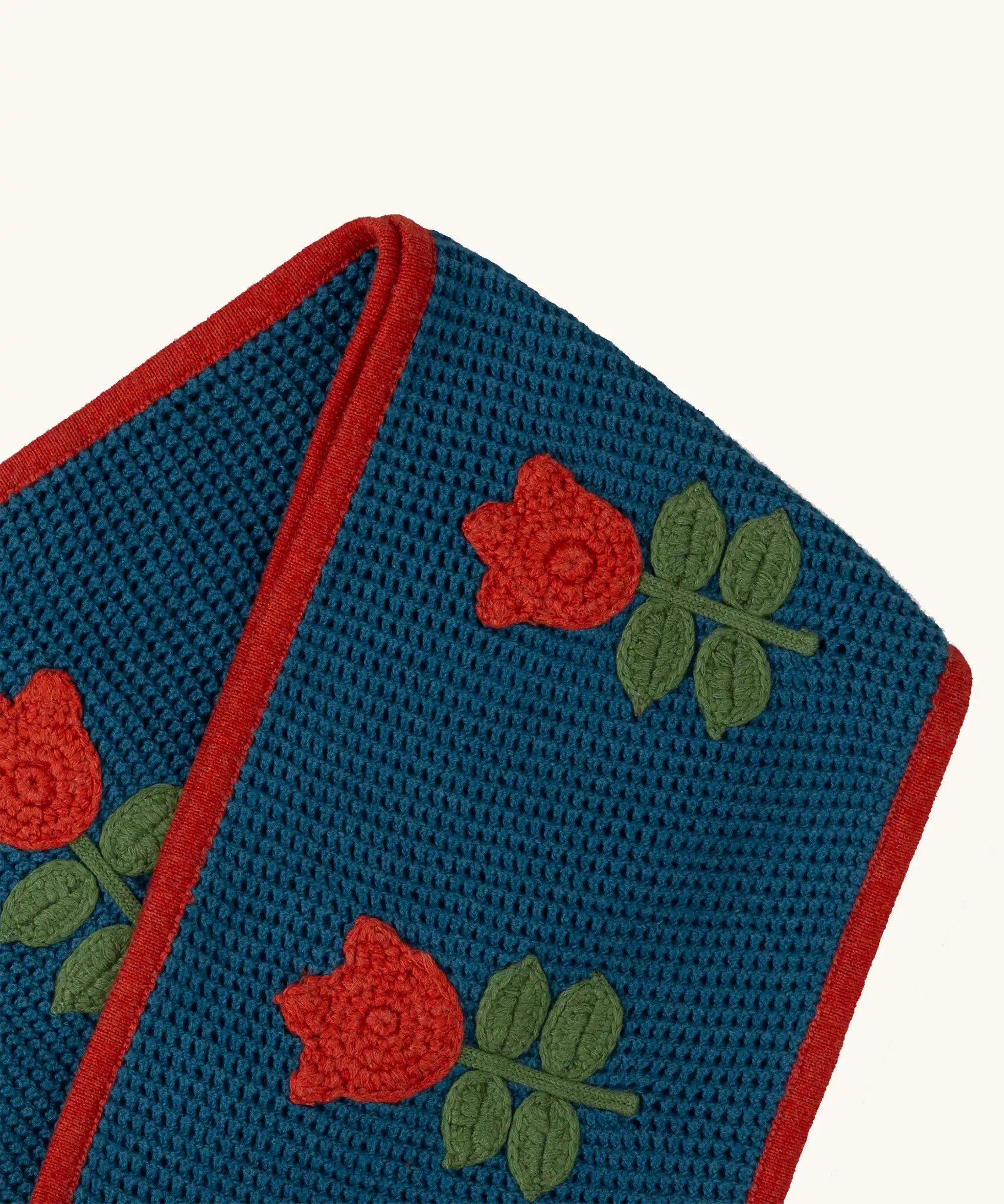 Close up of the Little Green Radicals tulips knitted blue scarf. Blue scarf with red tulips and red trim.