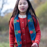 Child wearing Little Green Radicals tulips knitted blue scarf. Blue scarf with red tulips.