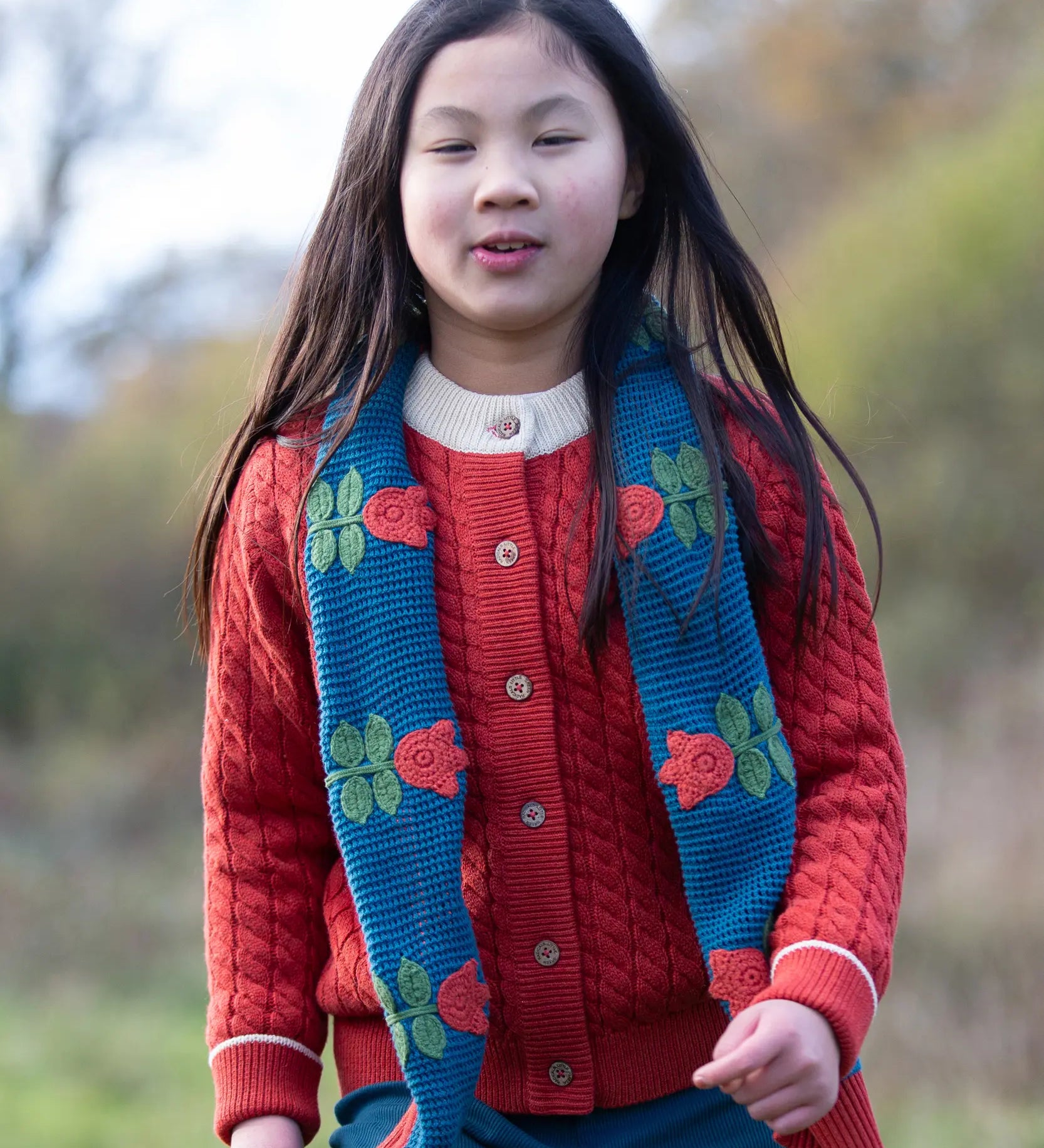 Child wearing Little Green Radicals tulips knitted blue scarf. Blue scarf with red tulips.