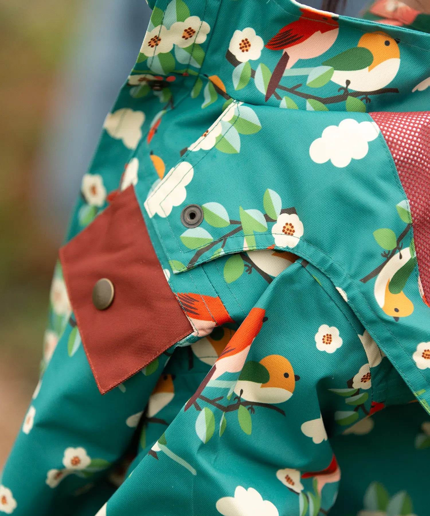 Close up of the popper closure on the hood of the Little Green Radicals turquoise birds recycled waterproof kids raincoat. Repeat pattern featuring bird on blossom branches.