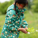 A child wearing the Little Green Radicals turquoise birds recycled waterproof kids raincoat. Repeat pattern featuring bird on blossom branches.