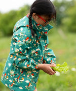 A child wearing the Little Green Radicals turquoise birds recycled waterproof kids raincoat. Repeat pattern featuring bird on blossom branches.