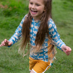 A child wearing the Little Green Radicals Children's Blue Whales design UPF 50+ Sunsafe Long Sleeve Rash Vest with yellow gold swim shorts.