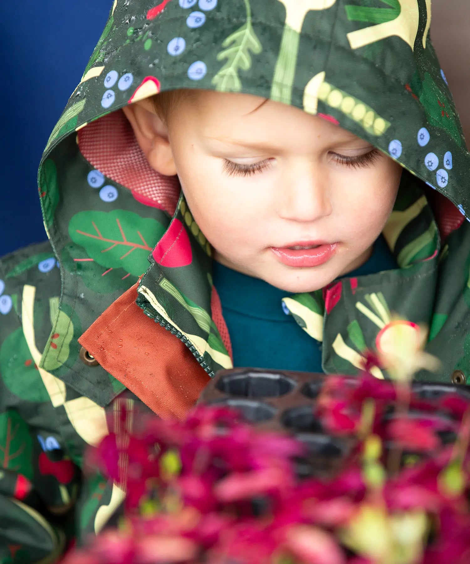 Close up of a child wearing the Little Green Radicals feast waterproof recycled kids raincoat with the hood up.