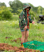 Child wearing the Little Green Radicals feast waterproof recycled kids raincoat with blue pinstripe shorts underneath with yellow wellington boots. 