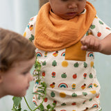 Close up of the repeat pattern print featuring nature themed illustrations top from the Little Green Radicals vintage style rainbows organic cotton t-shirt & jogger playset being worn by a toddler. 