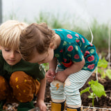 Close up of the Little Green Radicals weather knee patch blue and cream striped organic cotton joggers worn with a green apple print t-shirt and yellow wellington boots.