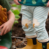 Close up of Little Green Radicals weather knee patch blue and cream striped organic cotton joggers being worn with yellow wellington boots. 