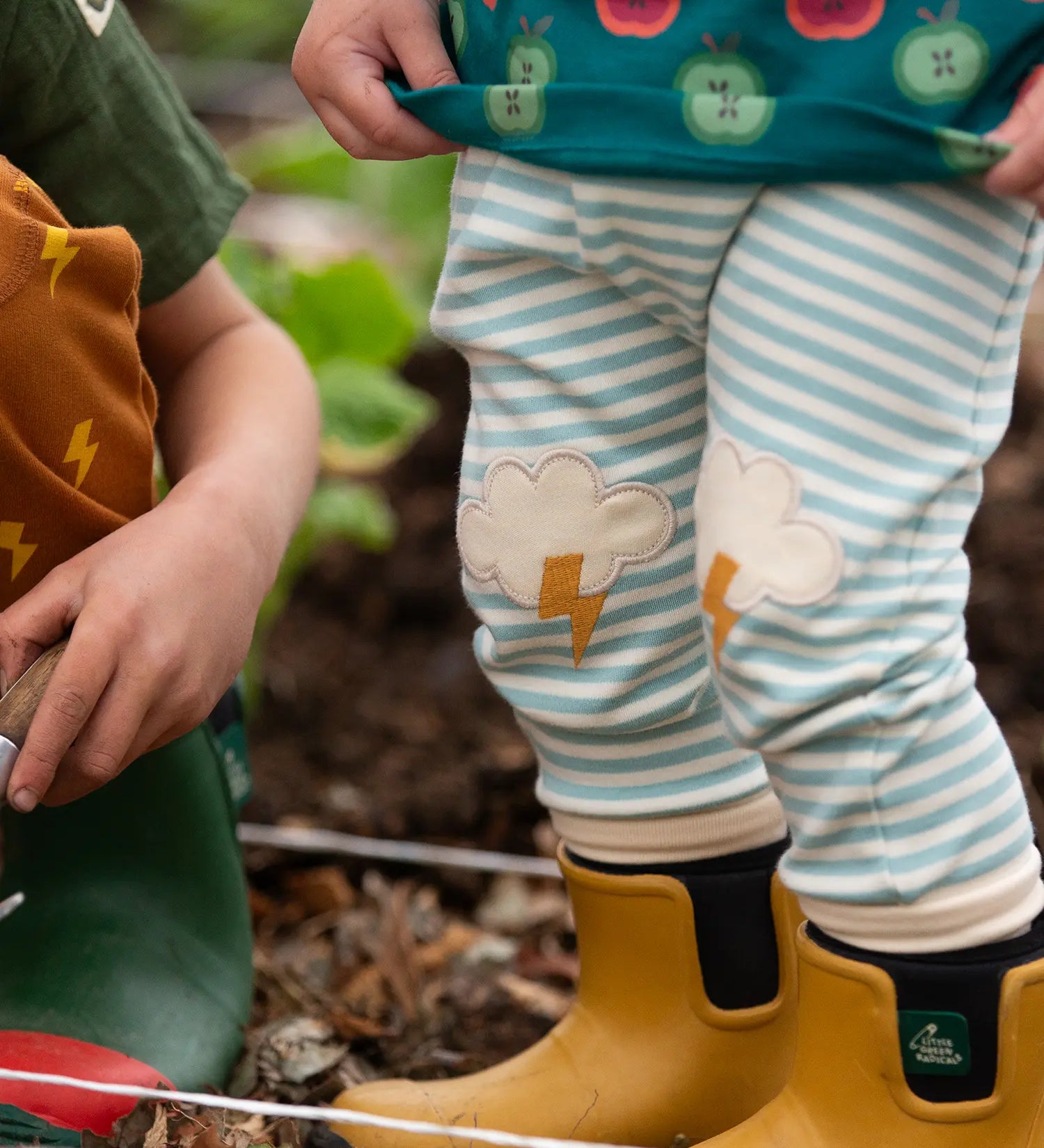 Close up of Little Green Radicals weather knee patch blue and cream striped organic cotton joggers being worn with yellow wellington boots. 