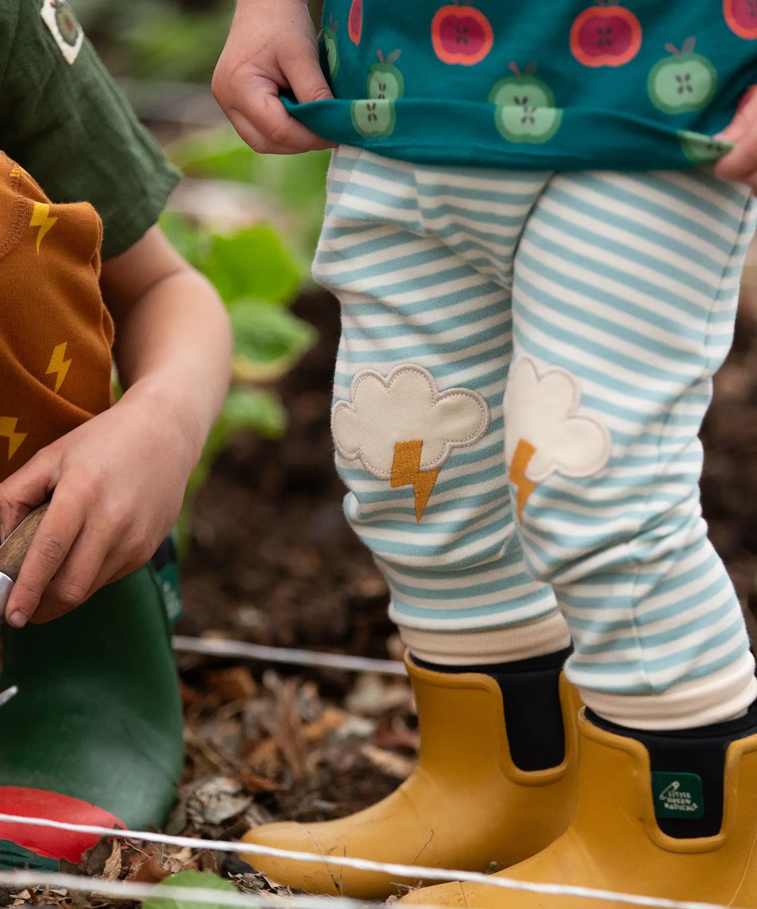 Close up of Little Green Radicals weather knee patch blue and cream striped organic cotton joggers being worn with yellow wellington boots. 