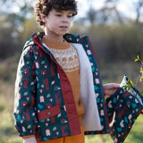 Child holding a Little Green Radicals  woodland print green recycled waterproof wet bag wearing a coat in the same print.