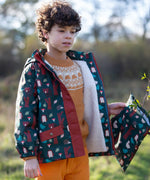 Child holding a Little Green Radicals  woodland print green recycled waterproof wet bag wearing a coat in the same print.