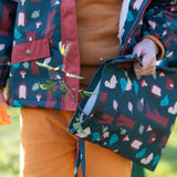 Child holding a Little Green Radicals  woodeland print green recycled waterproof wet bag wearing a coat and gloves in the same print.