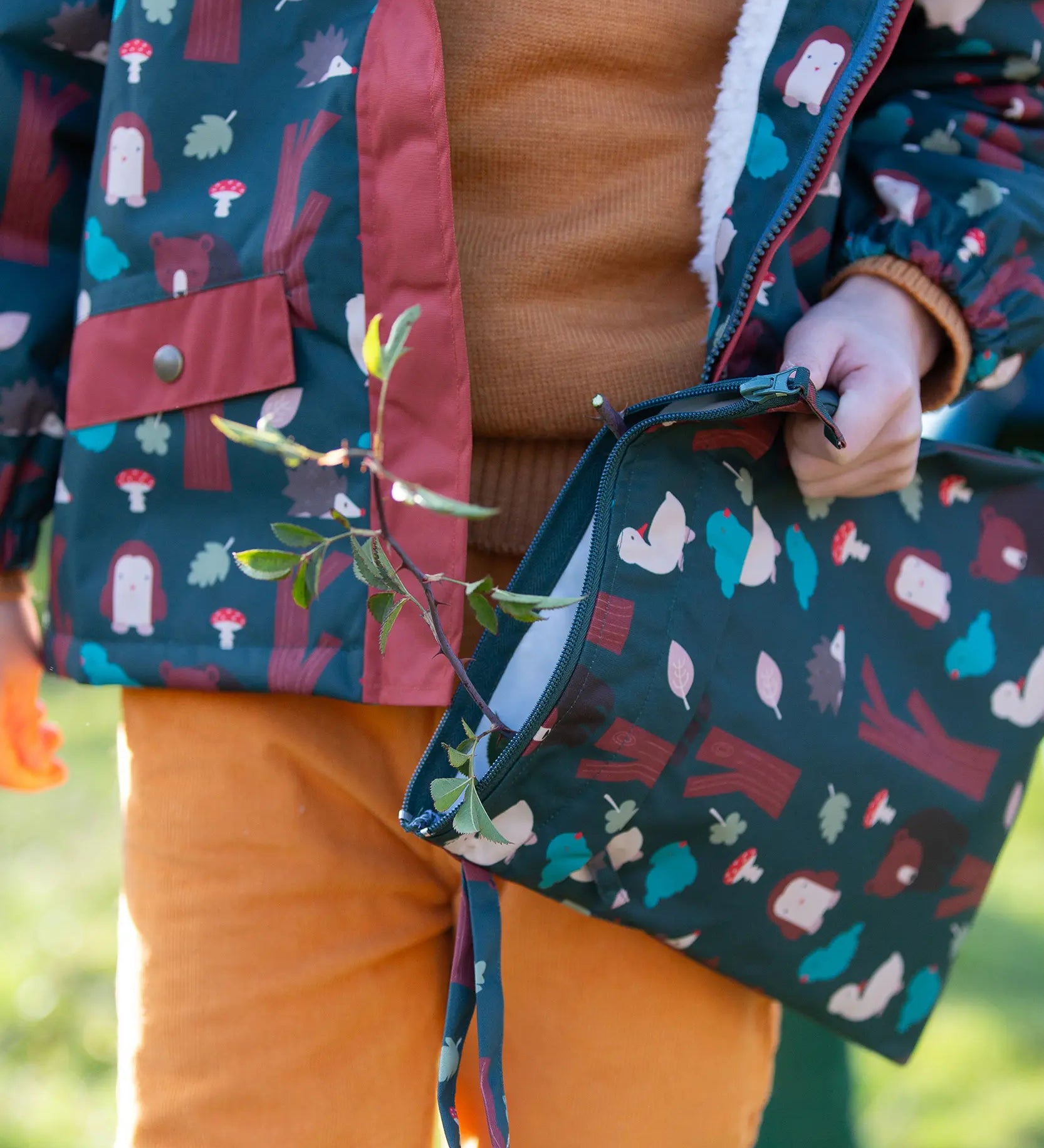Child holding a Little Green Radicals  woodeland print green recycled waterproof wet bag wearing a coat and gloves in the same print.