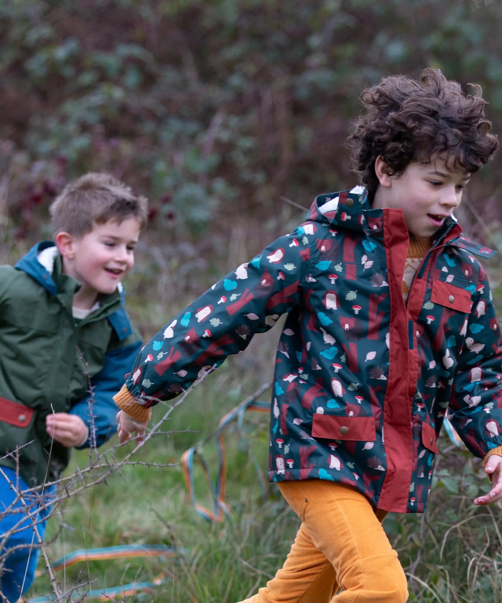 Child wearing a Little Green Radicals woodland world green recycled waterproof adventure winter coat with yellow gold trousers.