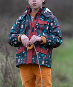 Child wearing a Little Green Radicals woodland world green recycled waterproof adventure winter coat with yellow gold trousers.