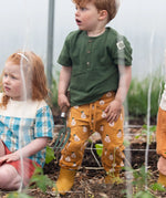 Child wearing the Little Green Radicals yellow gold comfy organic cotton kids joggers with a green muslin henley t-shirt and yellow wellington boots.