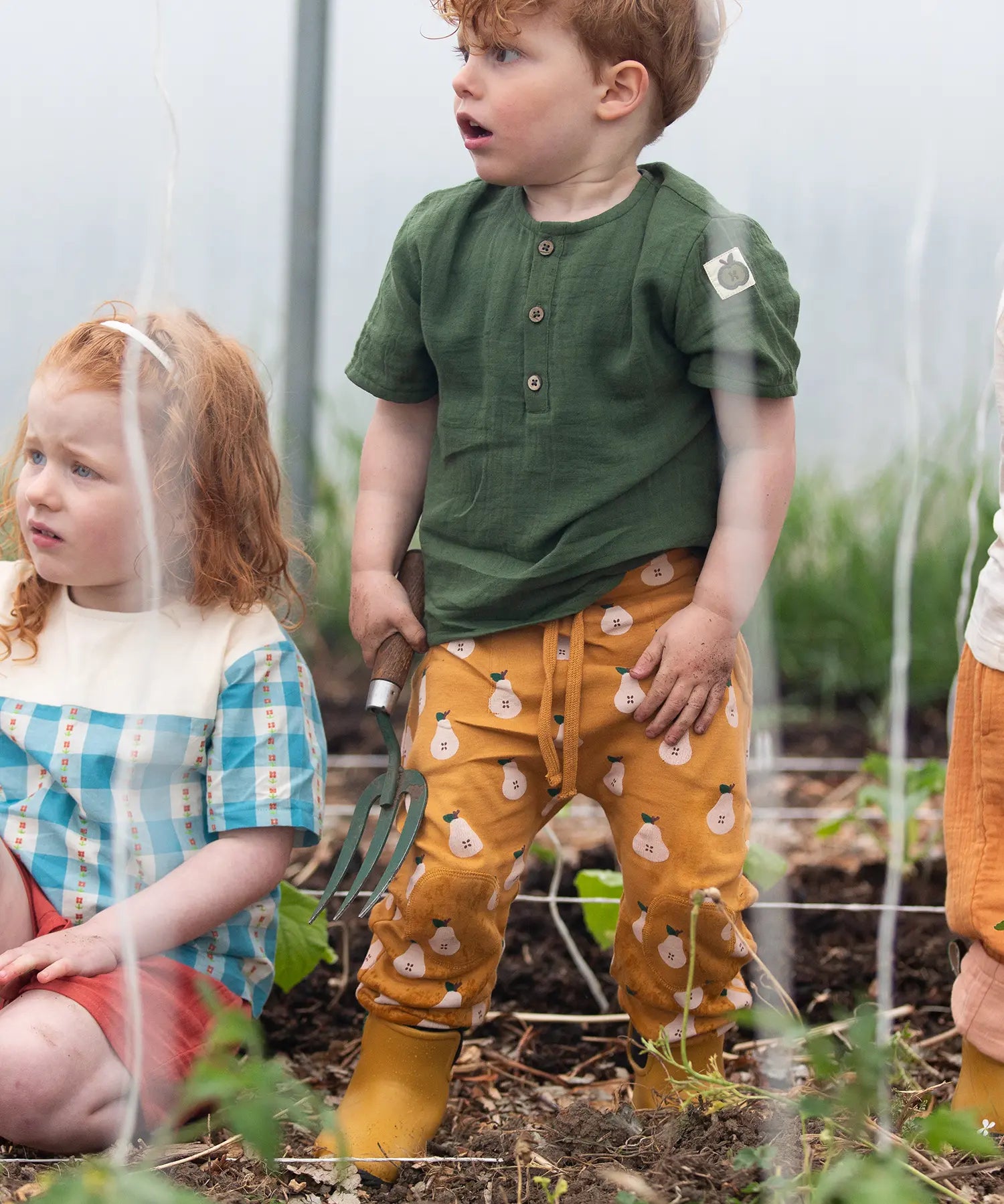 Child wearing the Little Green Radicals yellow gold comfy organic cotton kids joggers with a green muslin henley t-shirt and yellow wellington boots.