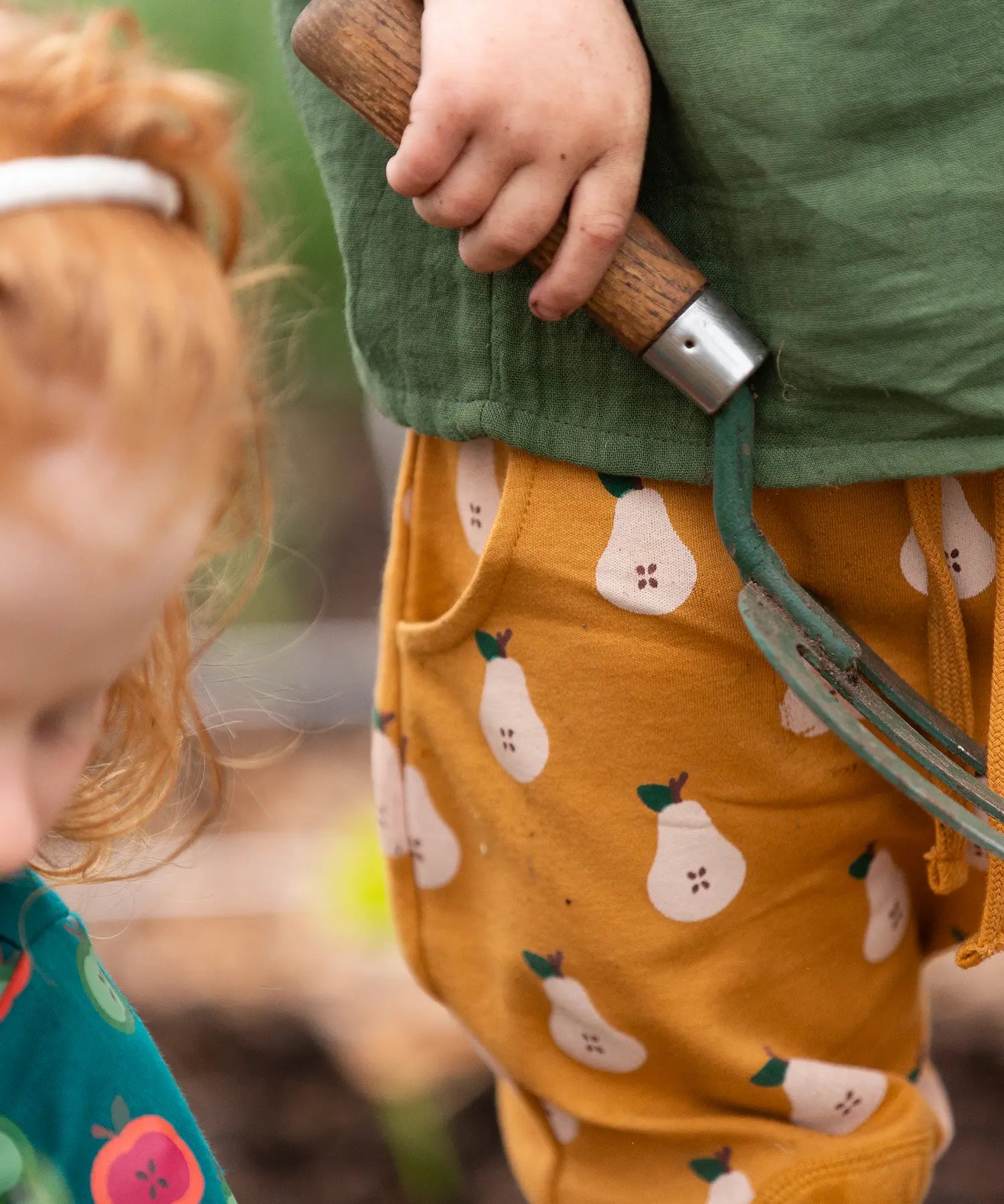 Close up of a child wearing the Little Green Radicals yellow gold comfy organic cotton kids joggers with a green muslin henley t-shirt.