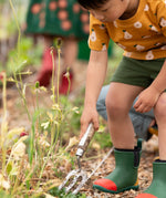 Child wearing the Little Green Radicals yellow gold summer pears short sleeve organic cotton t-shirt with green muslin shorts and green and red wellington boots. 