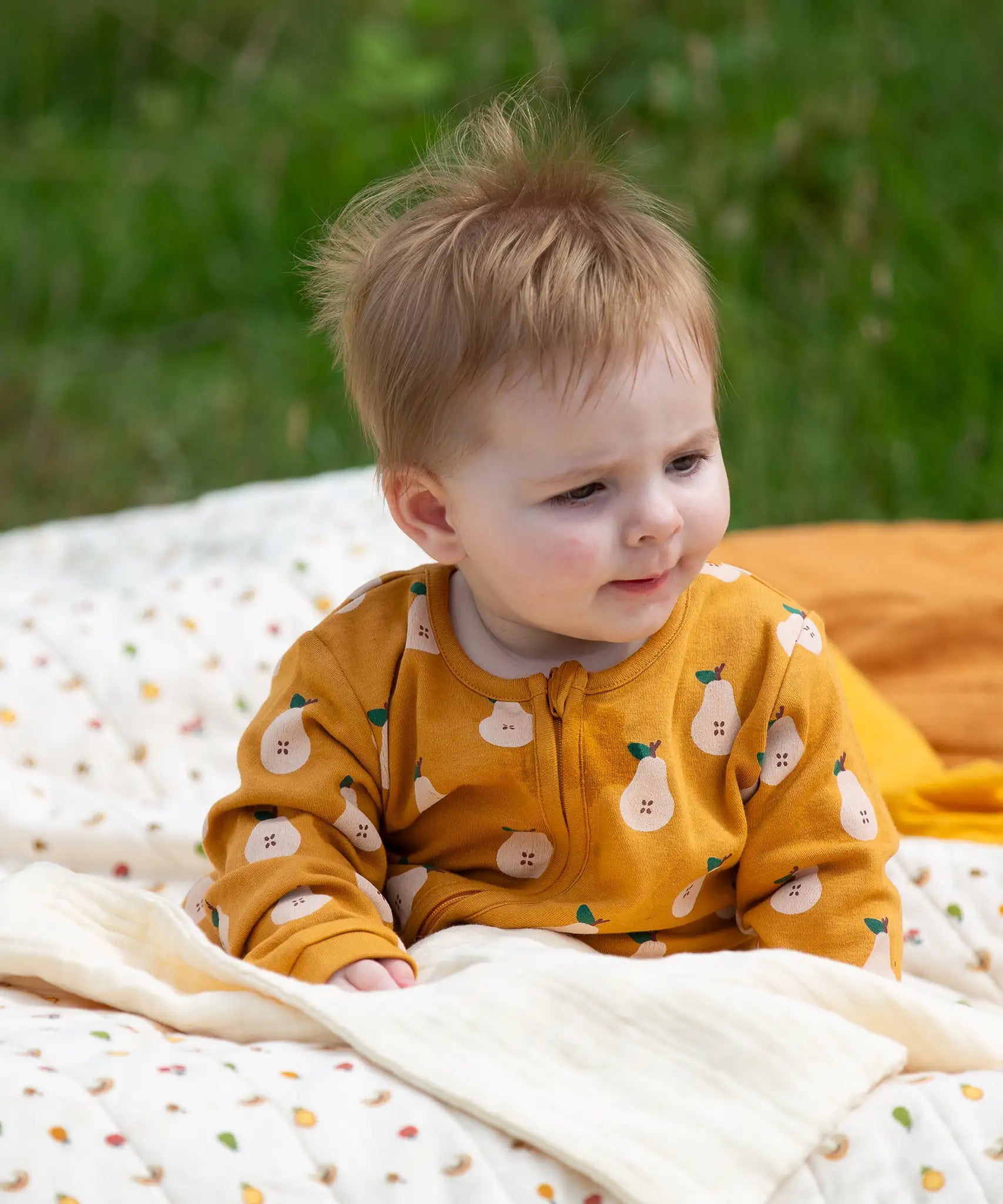 Little Green Radicals zip organic cotton footed babygrow with summer pears repeat print on a baby.