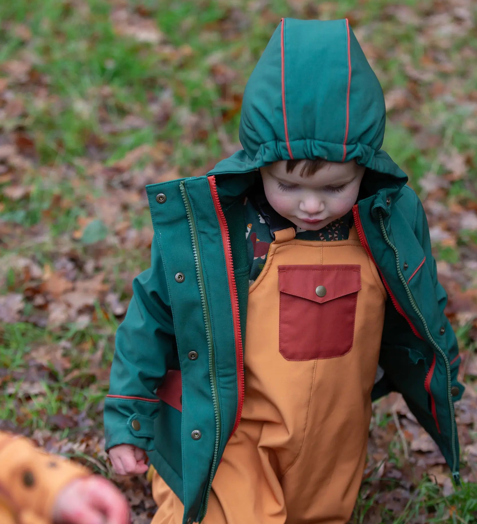 Child wearing the Little Green Radicals yellow gold recycled lined waterproof dungarees with a green coat.  
