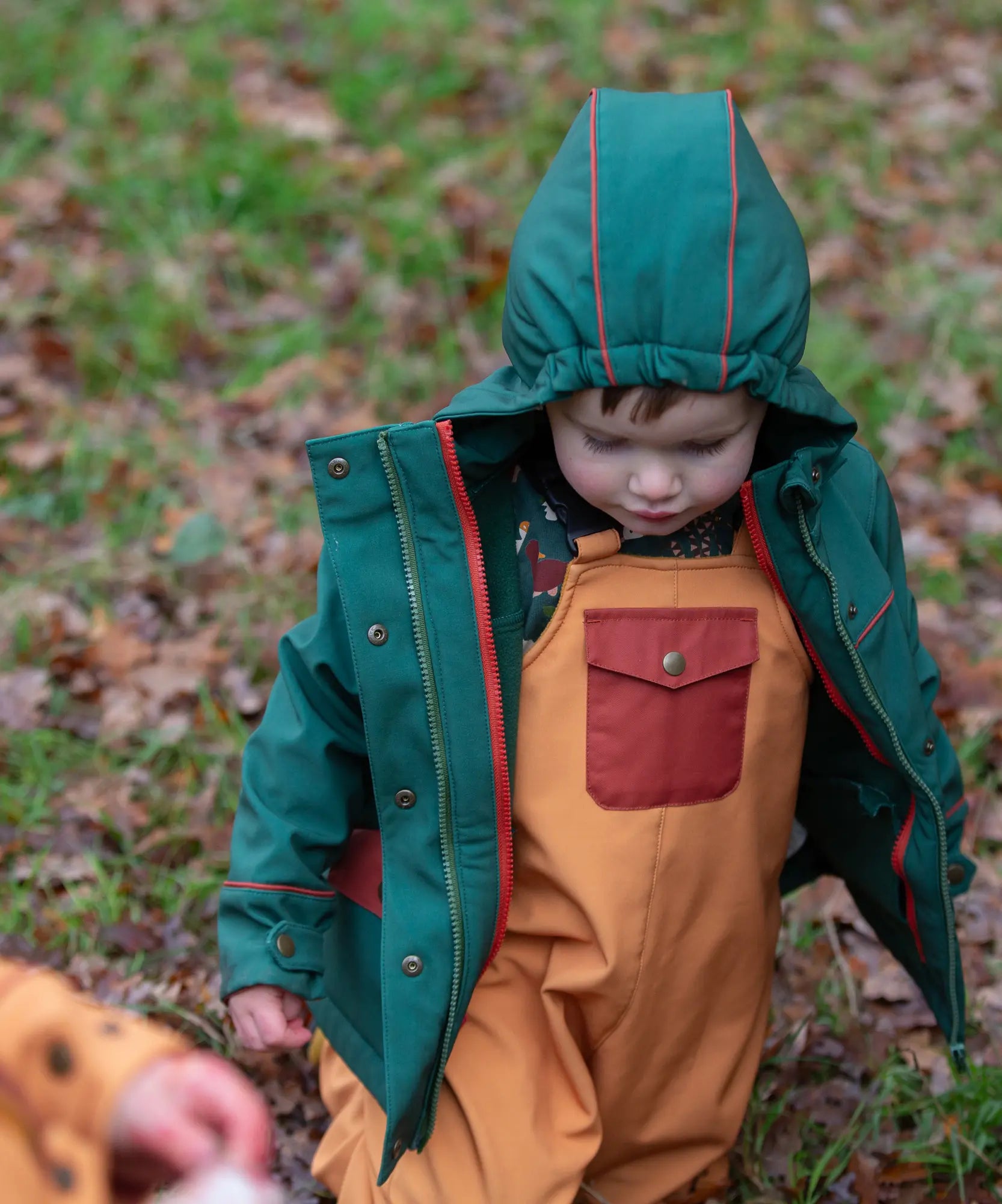 Child wearing the Little Green Radicals yellow gold recycled lined waterproof dungarees with a green coat.  