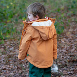 Back of a child wearing a Little Green Radicals yellow gold recycled waterproof 3 in 1 coat with green waterproof dungarees underneath.