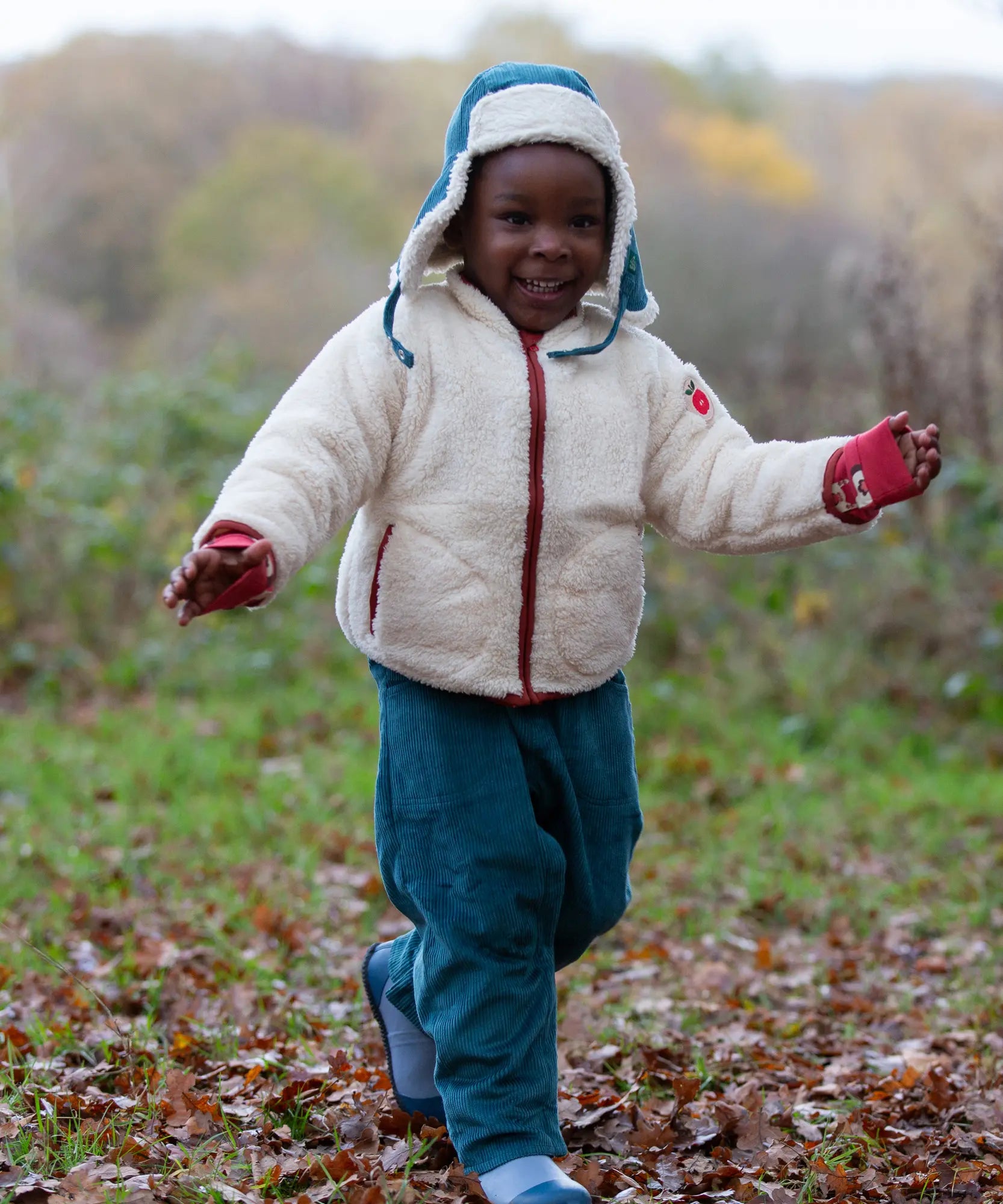 Child wearing the fleece jacket layer from the Little Green Radicals  yellow gold recycled waterproof 3 in 1 coat with blue corduroy trousers.