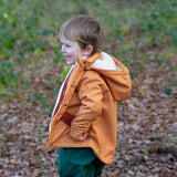 Side of a child wearing a Little Green Radicals yellow gold recycled waterproof 3 in 1 coat with green waterproof dungarees underneath.
