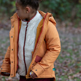 Child wearing a Little Green Radicals  yellow gold recycled waterproof 3 in 1 coat with berry purple trousers. The front zip is fully open.