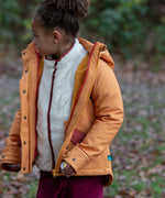 Child wearing a Little Green Radicals  yellow gold recycled waterproof 3 in 1 coat with berry purple trousers. The front zip is fully open.
