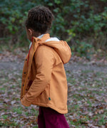 Child wearing a Little Green Radicals  yellow gold recycled waterproof 3 in 1 coat with berry purple trousers. Side view.