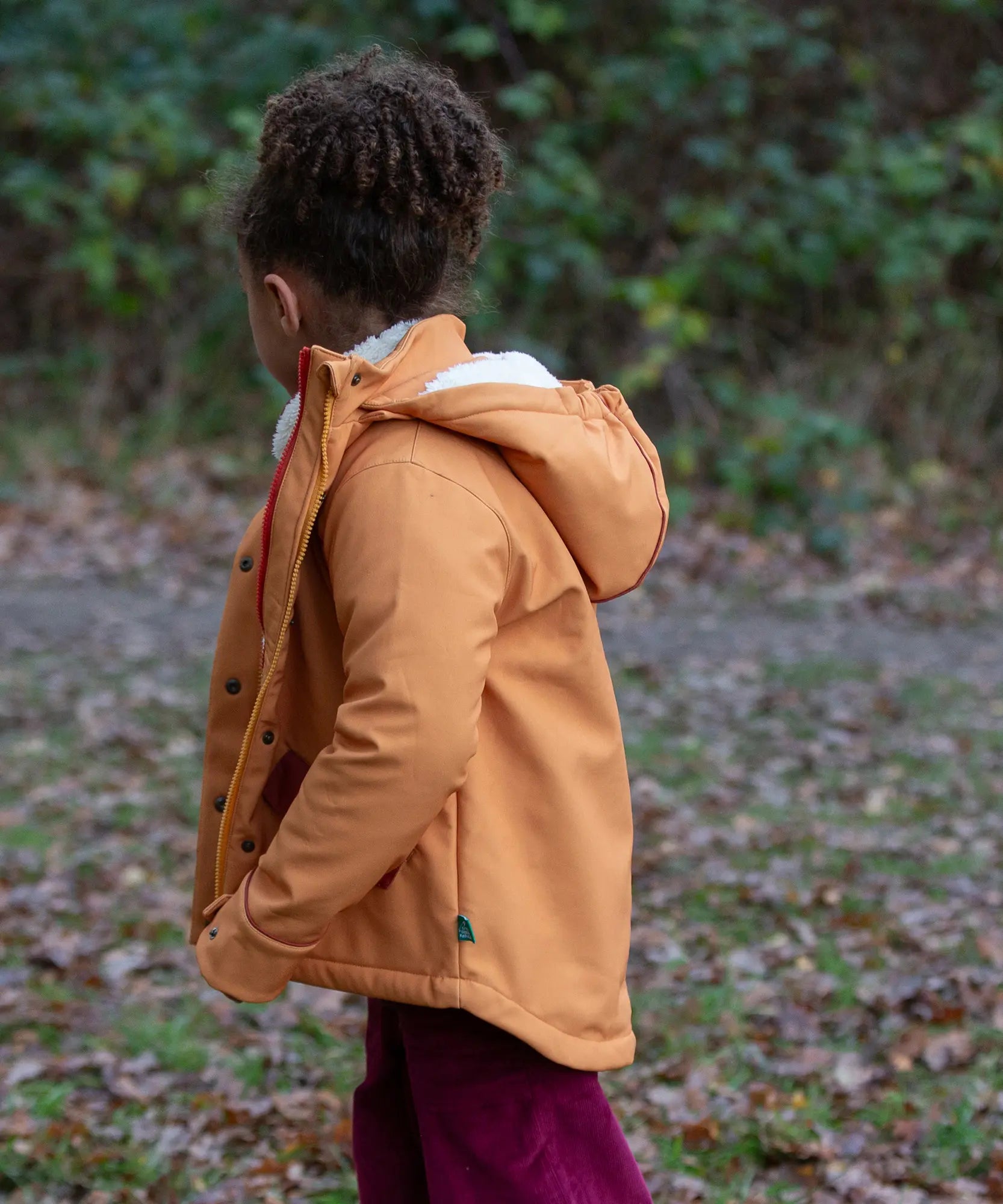 Child wearing a Little Green Radicals  yellow gold recycled waterproof 3 in 1 coat with berry purple trousers. Side view.