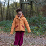 Child wearing a Little Green Radicals  yellow gold recycled waterproof 3 in 1 coat with berry purple trousers.