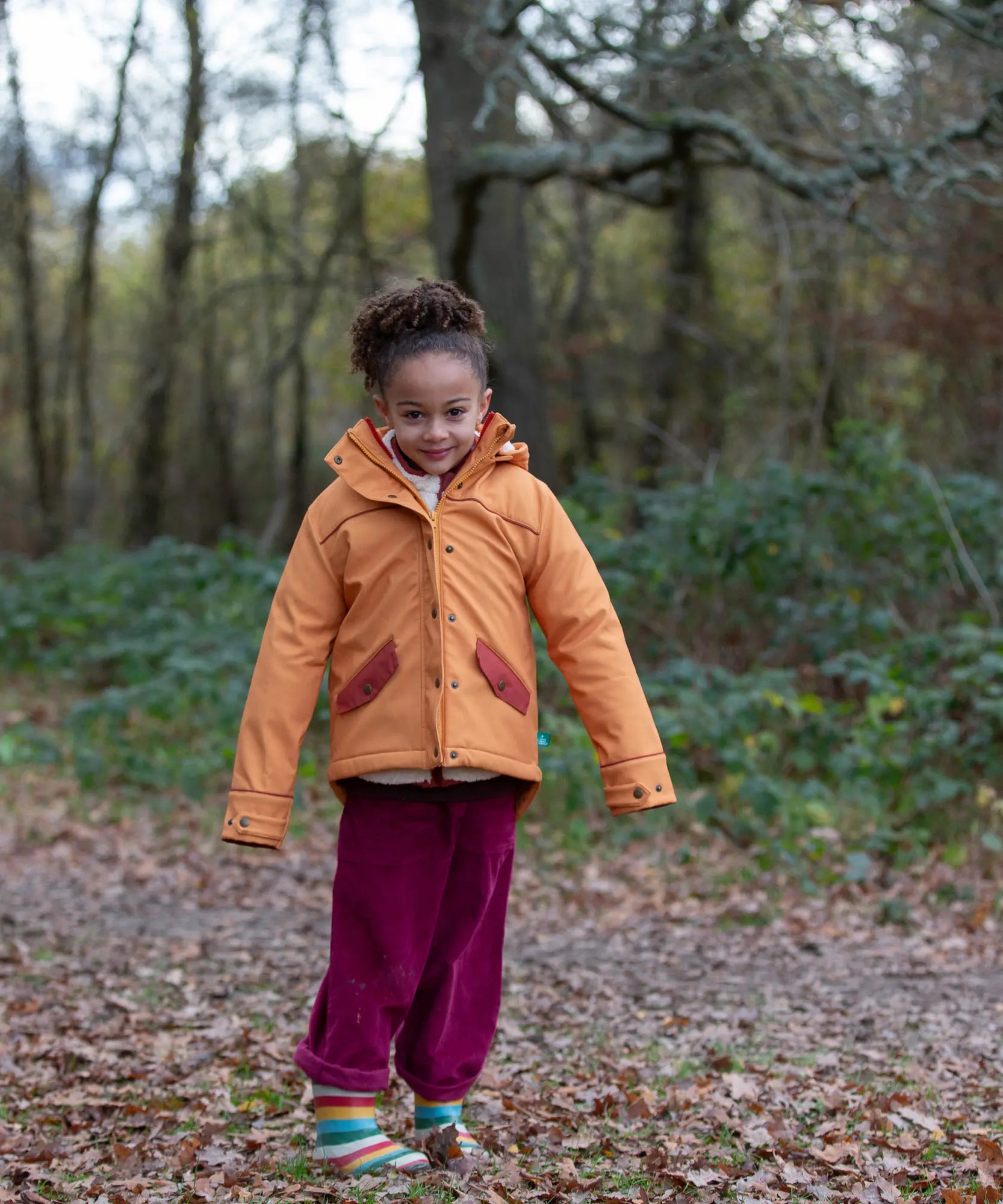 Child wearing a Little Green Radicals  yellow gold recycled waterproof 3 in 1 coat with berry purple trousers.