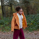 Child wearing a Little Green Radicals  yellow gold recycled waterproof 3 in 1 coat with berry purple trousers. The front zip is fully open.