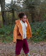 Child wearing a Little Green Radicals  yellow gold recycled waterproof 3 in 1 coat with berry purple trousers. The front zip is fully open.