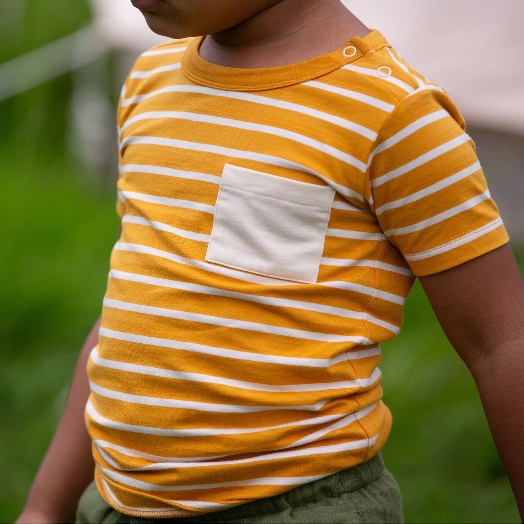 A close up of a child wearing the yellow gold striped Little Green Radicals from the Blue Organic T-Shirt Set.