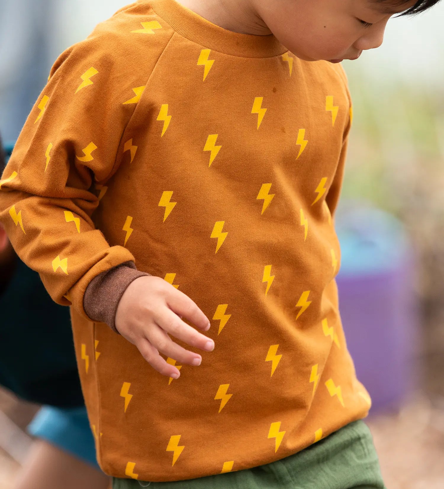 Close up of child wearing the Little Green Radicals kids yellow lightning print organic cotton sweatshirt.