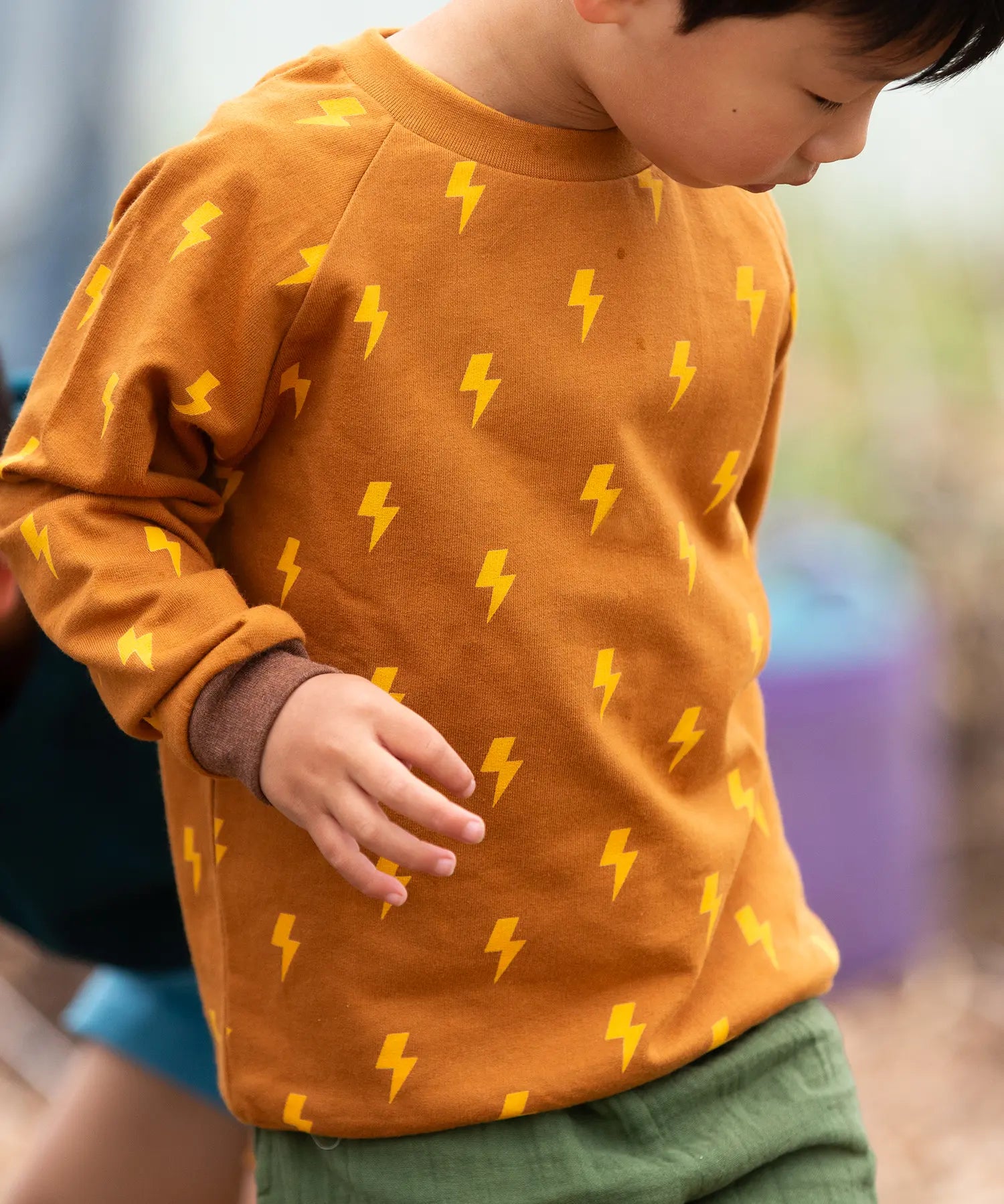 Close up of child wearing the Little Green Radicals kids yellow lightning print organic cotton sweatshirt.