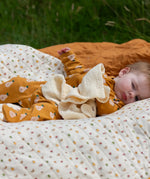 Little Green Radicals summer pears repeat print zip organic cotton footed babygrow on a baby laying on a patterned blanket. 