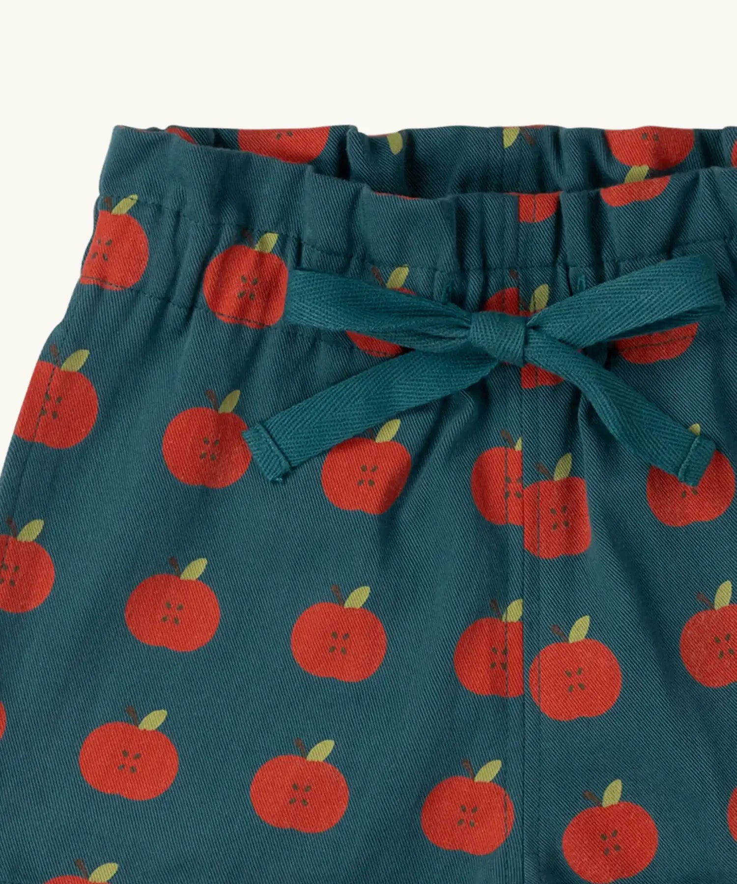 Close up of the waistband and tie on the Little Green Radicals blue kids organic cotton shorts with repeat apple print all over. 
