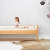 A child is seen lying on a bed which has a Little Green Sheep Organic Junior Mattress Protector placed on the matress