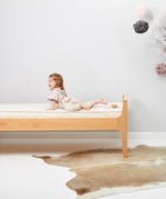 A child is seen lying on a bed which has a Little Green Sheep Organic Junior Mattress Protector placed on the matress